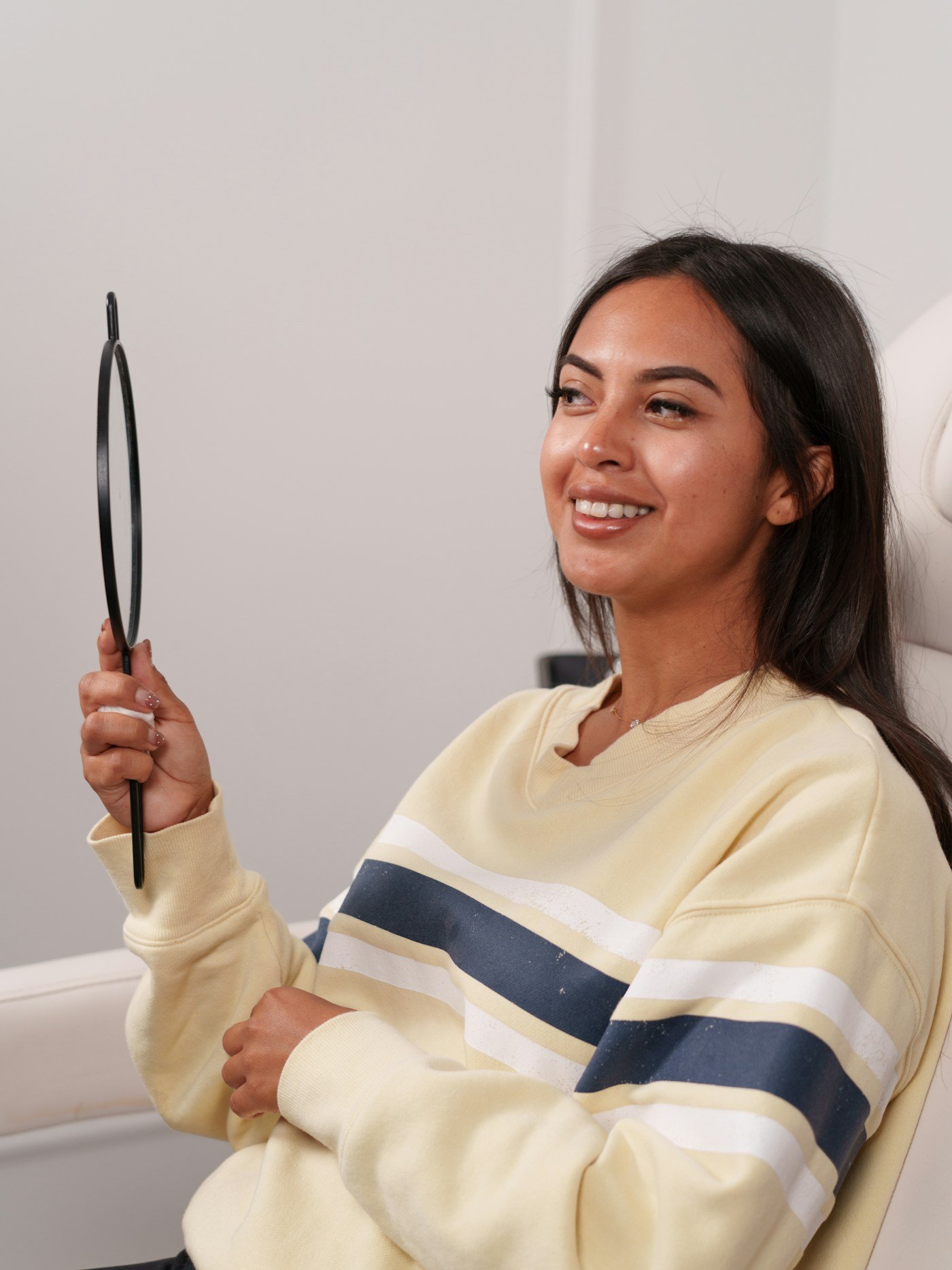 A smiling patient checks her teeth in a hand mirror after a cleaning